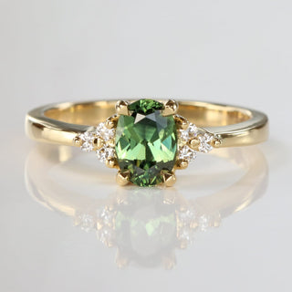 Handmade 18ct yellow gold engagement ring with a natural unheated oval Parti sapphire and Canadian diamond cluster, photographed on a reflective surface.