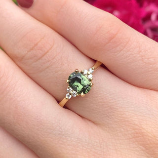 Oval Parti sapphire and diamond cluster engagement ring in handmade 18ct yellow gold shown on hand.