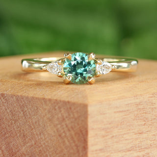 18ct gold Green sapphire and pear cut diamond trilogy ring on a wooden box with green background