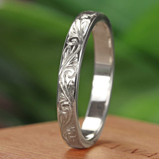Angled view of Platinum wedding band engraved with a floral scroll pattern on a wooden box with blurred green background