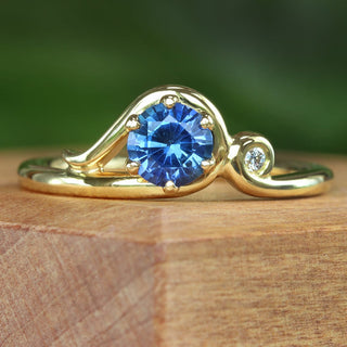 Blue sapphire engagement ring with Art Nouveau curl design photographed on wooden surface.