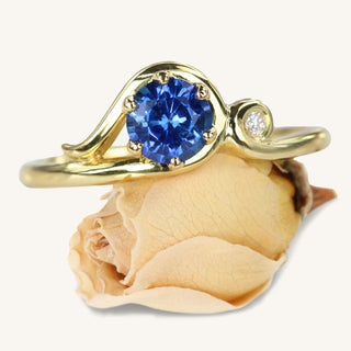 Ceylon sapphire Art Nouveau inspired engagement ring resting on a rose flower.
