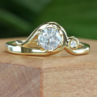 Handmade 18ct gold Art Nouveau engagement ring with icy diamond and accent diamond on natural wooden surface.