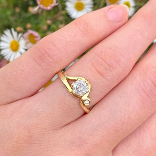Handmade 18ct gold ornate Art Nouveau inspired engagement ring, set with an icy natural diamond. Displayed being worn on the hand with daisy flowers in the background