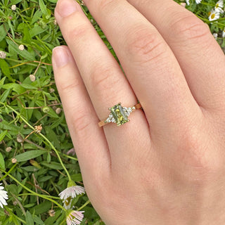 Handmade 18ct gold emerald cut green sapphire and cluster diamond engagement ring being worn on the hand