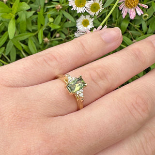 Closeup of 18ct gold fair trade radiant cut Parti sapphire and diamond cluster engagement ring, worn on the finger with daisy backdrop