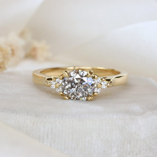 18ct gold cluster engagement ring with salt and pepper diamond photographed on pale fabric.