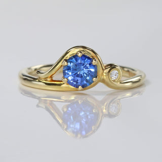 Handmade 18ct gold Art Nouveau sapphire engagement ring with Canadian diamond on reflective surface.