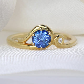 Blue sapphire Art Nouveau engagement ring photographed on pale fabric.