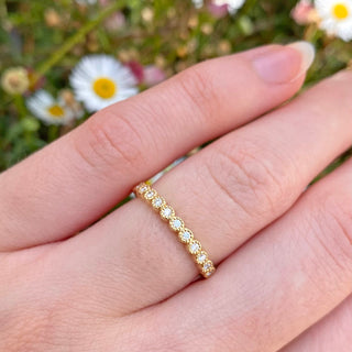 Handmade solid 18ct gold wedding or half eternity band, set with twelve fair trade natural white diamonds. Show being worn on the hand with daisy backdrop