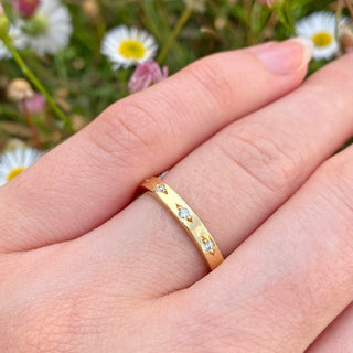 Handmade 2.5mm wide solid 18ct gold wedding ring with ten fair trade natural white diamonds spaced around the band, held in pretty bead settings. Show being worn on the hand with daisy backdrop