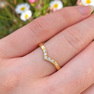 Handmade solid 18ct gold wishbone style wedding ring with five fair trade diamonds pave set into the front of the band. Shown being worn on the hand with daisies in the background