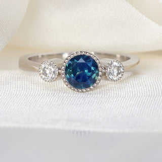 Natural unheated Parti sapphire trilogy engagement ring in platinum photographed on pale fabric.
