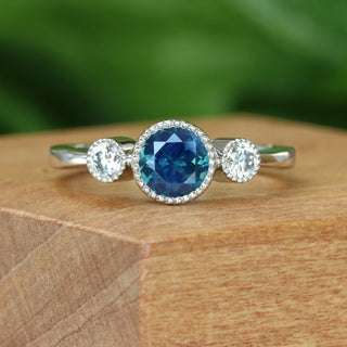 Handmade platinum Parti sapphire and diamond trilogy engagement ring on wooden surface.
