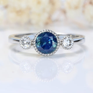 Handmade Parti sapphire and diamond trilogy ring in platinum on white background and faded floral backdrop.