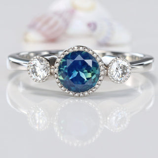 Close-up of platinum Parti sapphire and diamond trilogy ring on reflective background.
