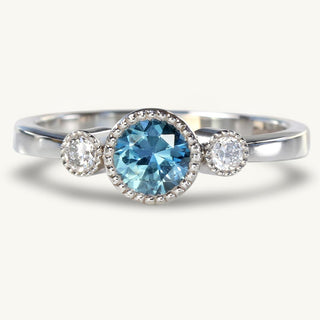 Platinum trilogy engagement ring with a fair trade blue sapphire and natural diamonds held in bezel setting with pretty milgrain edging