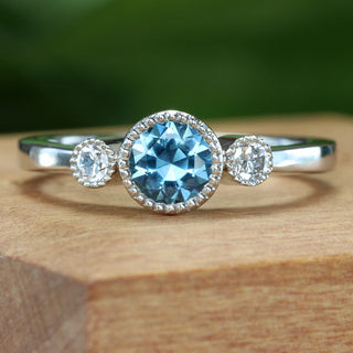 Platinum trilogy engagement ring with teal sapphire shown inside sustainable wooden ring box.
