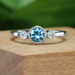 Platinum trilogy engagement ring with teal sapphire shown inside sustainable wooden ring box.