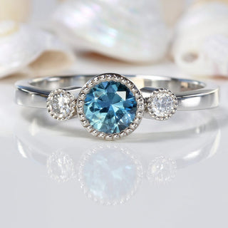 Platinum blue sapphire and diamond trilogy engagement ring on reflective background with seashells
