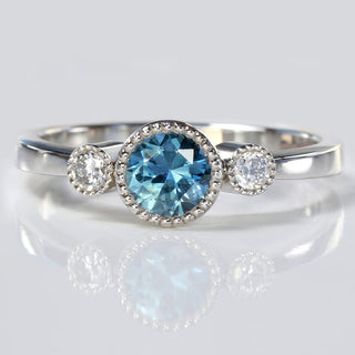 Platinum blue sapphire and diamond trilogy engagement ring on reflective background