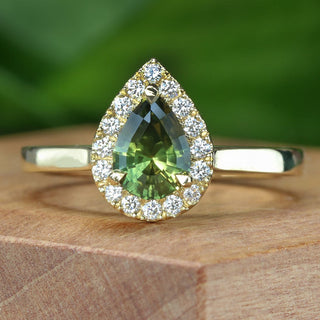 Handmade 18ct gold green sapphire halo engagement ring photographed on wooden surface.
