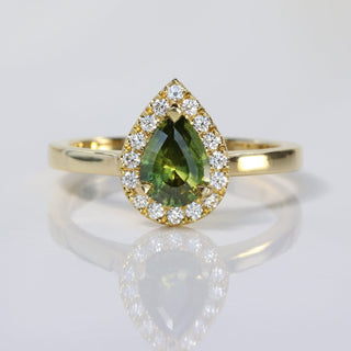 Handmade 18ct gold green sapphire halo engagement ring with Canadian diamonds on reflective surface.