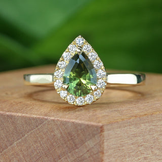 Handmade 18ct gold green sapphire halo engagement ring photographed on wooden surface.
