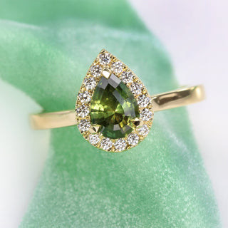 Front view of pear cut green sapphire and diamond halo engagement ring, handmade from 18ct gold on a green ribbon.