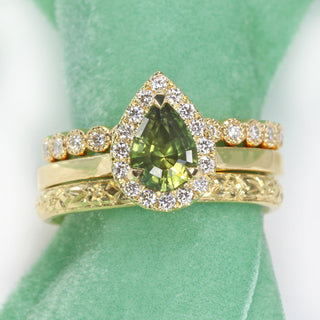 18ct gold green sapphire halo engagement ring paired with orange blossom engraved wedding ring and matching diamond eternity ring.