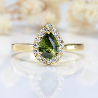 Green sapphire engagement ring with a halo of diamonds, on a soft white floral backdrop.