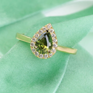 18ct gold green sapphire halo engagement ring photographed on green fabric at an angle.
