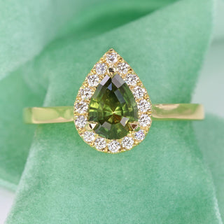 18ct gold green sapphire halo engagement ring photographed on green fabric.