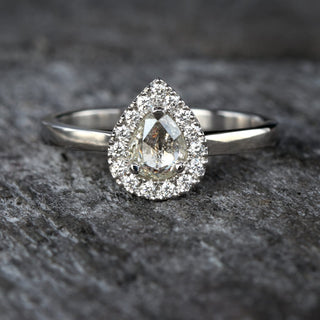 Platinum halo engagement ring with pear diamond photographed on dark textured background.