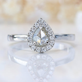 Front view of rose cut pear diamond halo ring photographed on pale floral background.