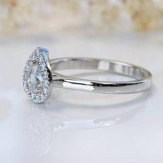 Side view of diamond halo platinum engagement ring with soft floral background.