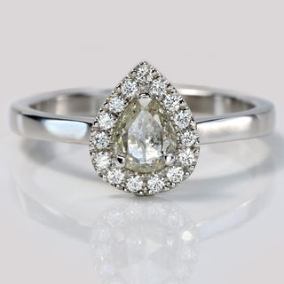 Handmade platinum pear diamond halo engagement ring with pavé setting on reflective surface.
