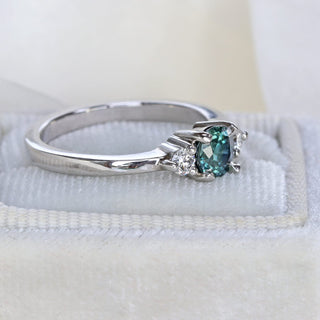 Platinum trilogy engagement ring with teal sapphire and diamonds photographed at an angle on neutral background.