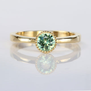 Handmade 18ct gold solitaire engagement ring with natural green sapphire in a milgrain bezel setting.