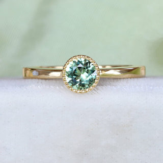 Handmade 18ct gold green sapphire solitaire engagement ring on pale textured fabric.