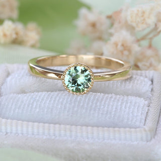 Close-up of handmade 18ct gold solitaire engagement ring with green sapphire in a milgrain bezel setting.