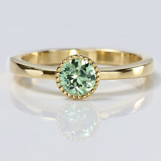 Green sapphire solitaire engagement ring handmade from 18ct gold on a white reflective background