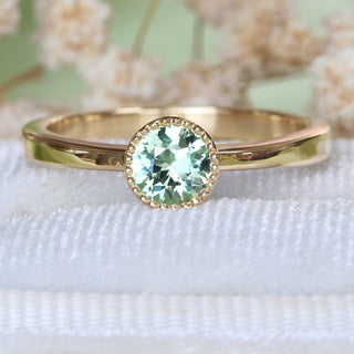 Close-up of handmade 18ct gold solitaire engagement ring with green sapphire in a milgrain bezel setting.