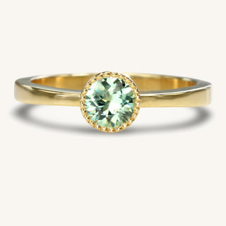 Handmade green sapphire solitaire ring in sustainable solid 18ct gold. The stone is held in a bezel setting with pretty milgrain detail