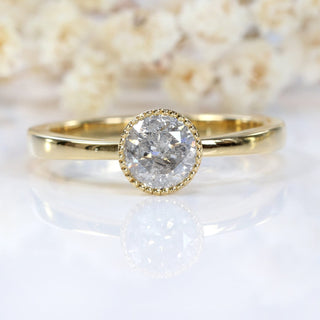 Close-up of 18ct gold salt and pepper diamond solitaire ring on pale floral background