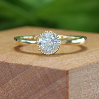 Salt and pepper diamond solitaire ring on wooden block with warm lighting.