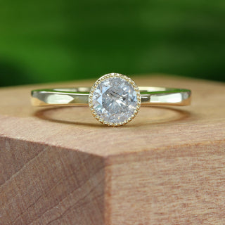 Salt and pepper diamond solitaire engagement ring photographed outdoors on a green background.