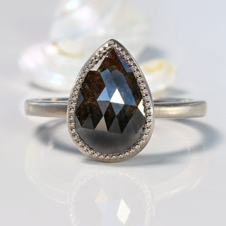 Pear cut black diamond solitaire ring made from 18ct white gold, on a reflective surface