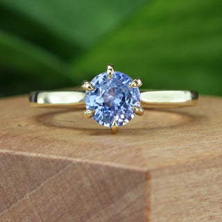 Lavender blue sapphire solitaire engagement ring on wooden ring box with green background