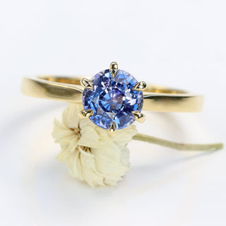 Lavender blue sapphire solitaire engagement ring resting on a white flower